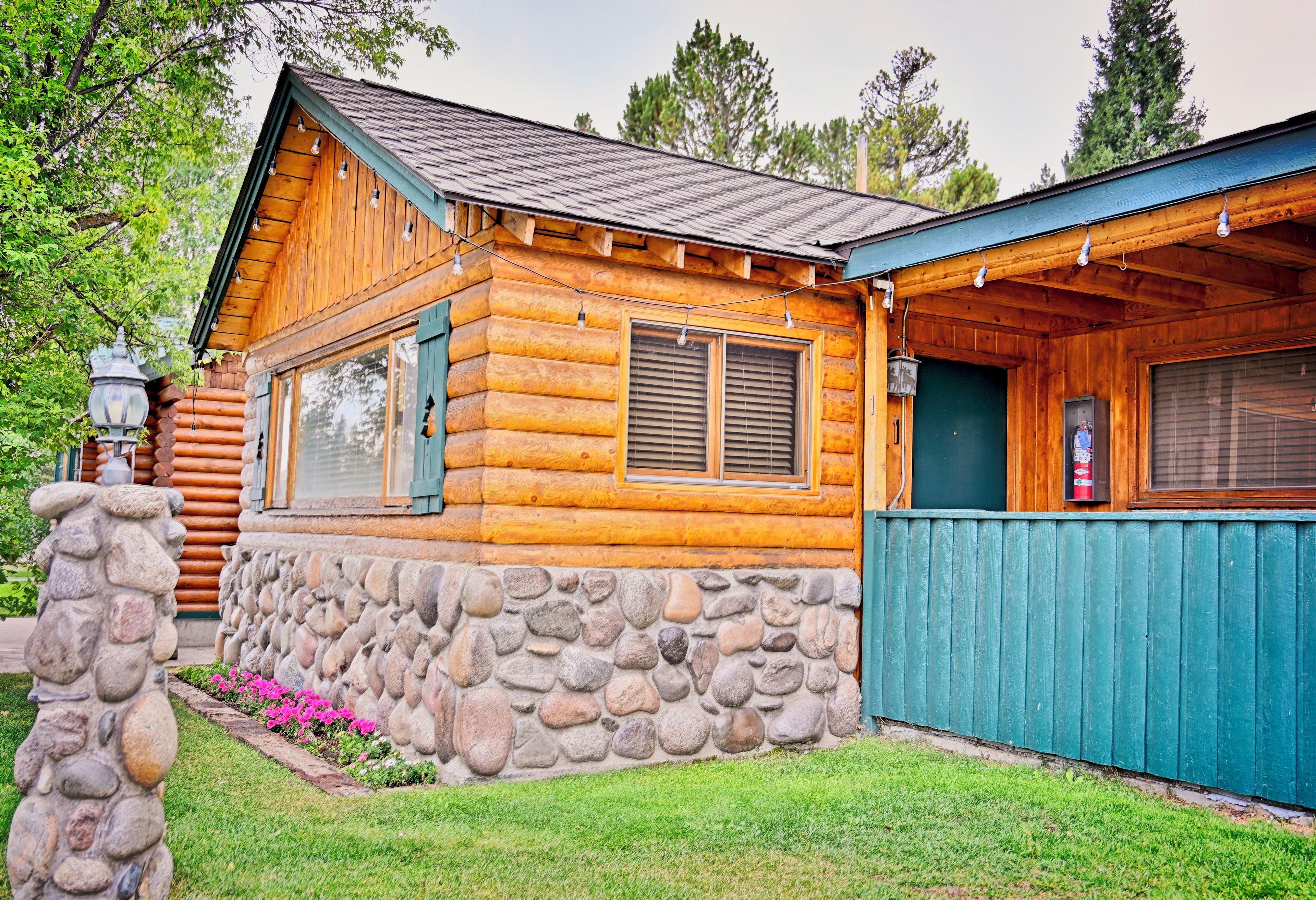 Una cabaña de troncos con cimientos de piedra, ventanas amplias y fachada verde.