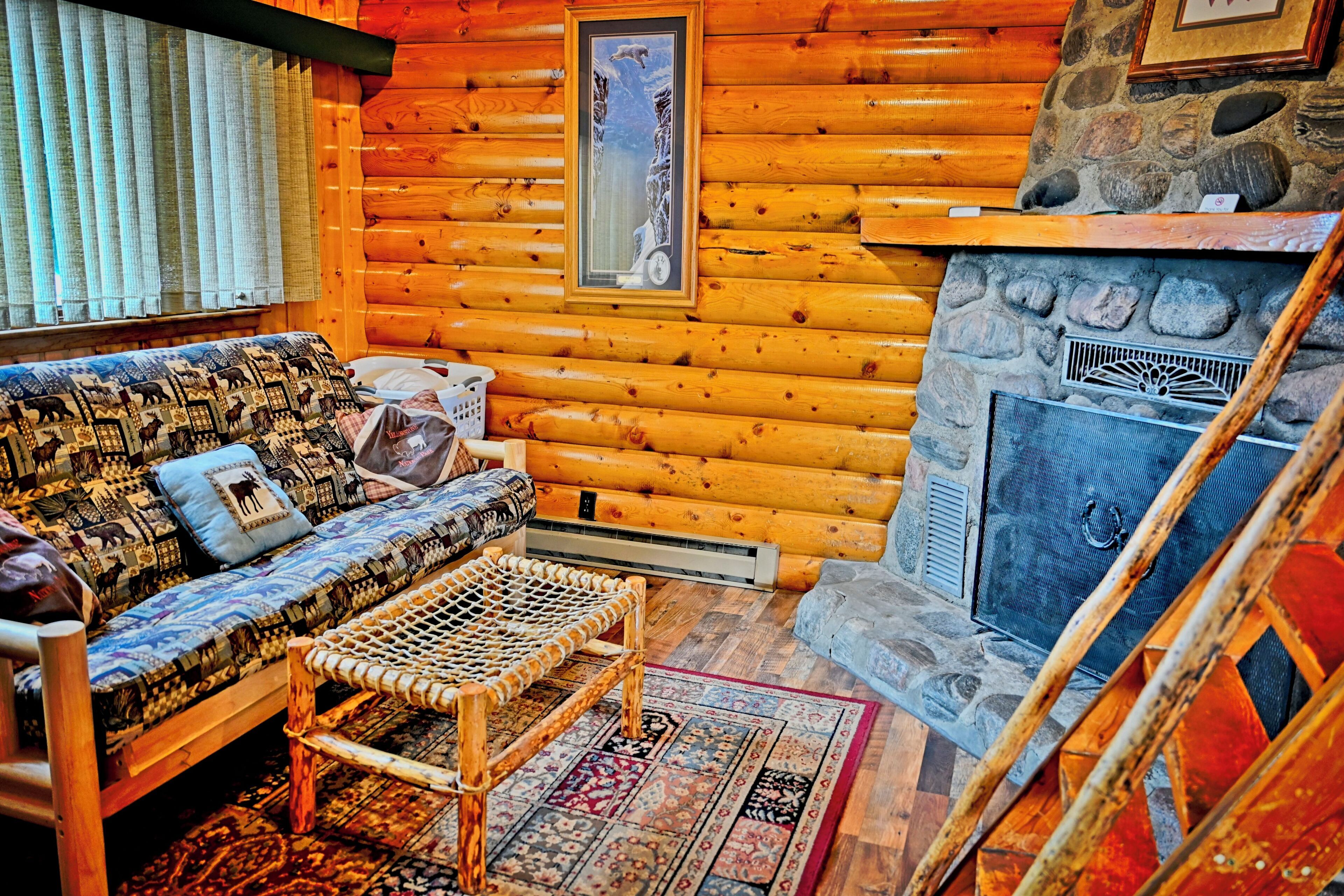 A log cabin interior with a sofa, a woven bench, a fireplace, and a stone wall.