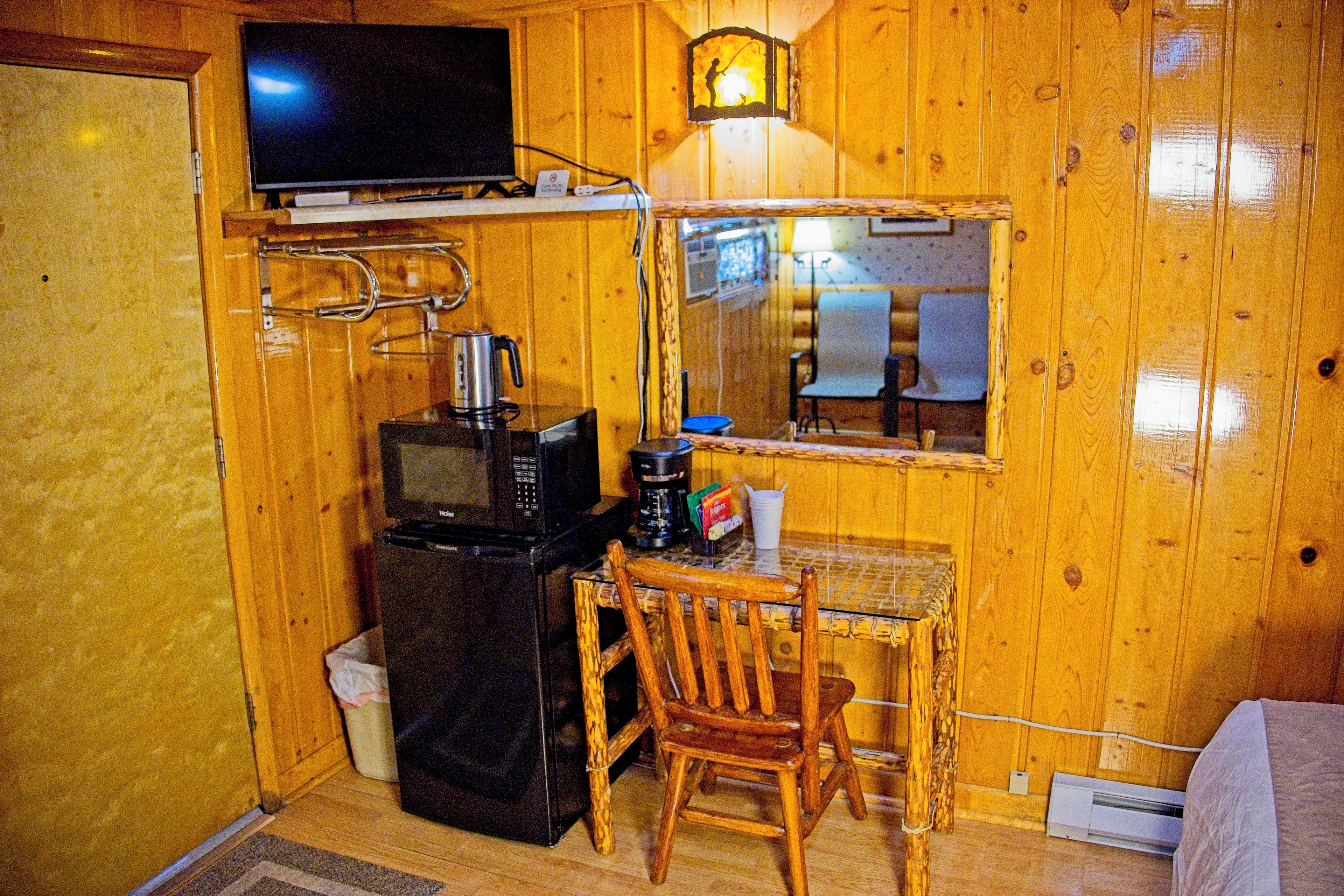 Una habitación compacta con televisión montada en la pared, una mesita con una silla, microondas y cafetera.