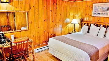 Una habitación de madera con una cama, un escritorio, una silla, una lámpara y un cuadro en la pared.