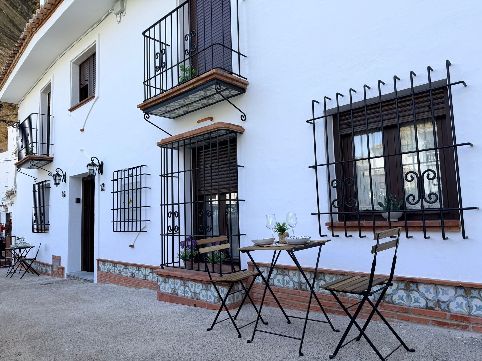 A white building with black metal railings, a small table with chairs, and a potted plant.