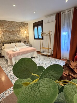 A hotel room with a bed, a wooden wall, a window with curtains, and a hanging laundry rack. - The Jewel of Setenil - Rubí Cave House (Setenil de las Bodegas)