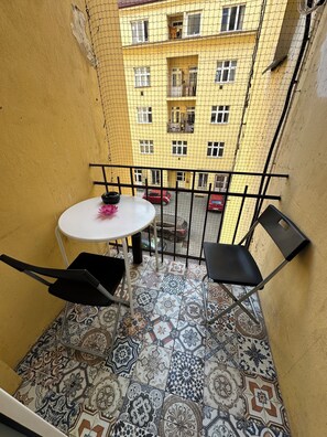 Un balcon avec une table blanche, deux chaises noires et des carreaux de sol à motifs.