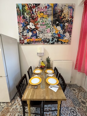 A dining area with a wooden table set for four, surrounded by chairs. Above the table is a colorful abstract painting. - Cozy Karlín 2BR Loft III Metro 1 Min (prague)