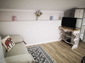 A living room with a sofa, a TV on a stand, a patterned rug, and a wall-mounted shelf with decorative items. - Feather House FH Wine Cellar (São Bartolomeu de Galegos)