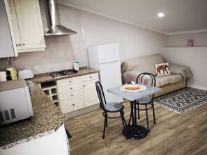 Una cocina compacta con estufa a gas, un refrigerador blanco y un comedor con mesa y sillas.