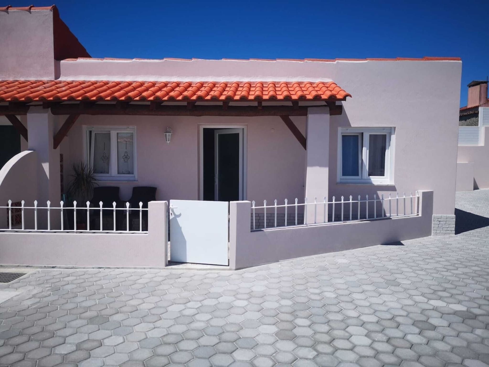 A modern building with a red-tiled roof, a white fence, and a hexagonal tile pavement.