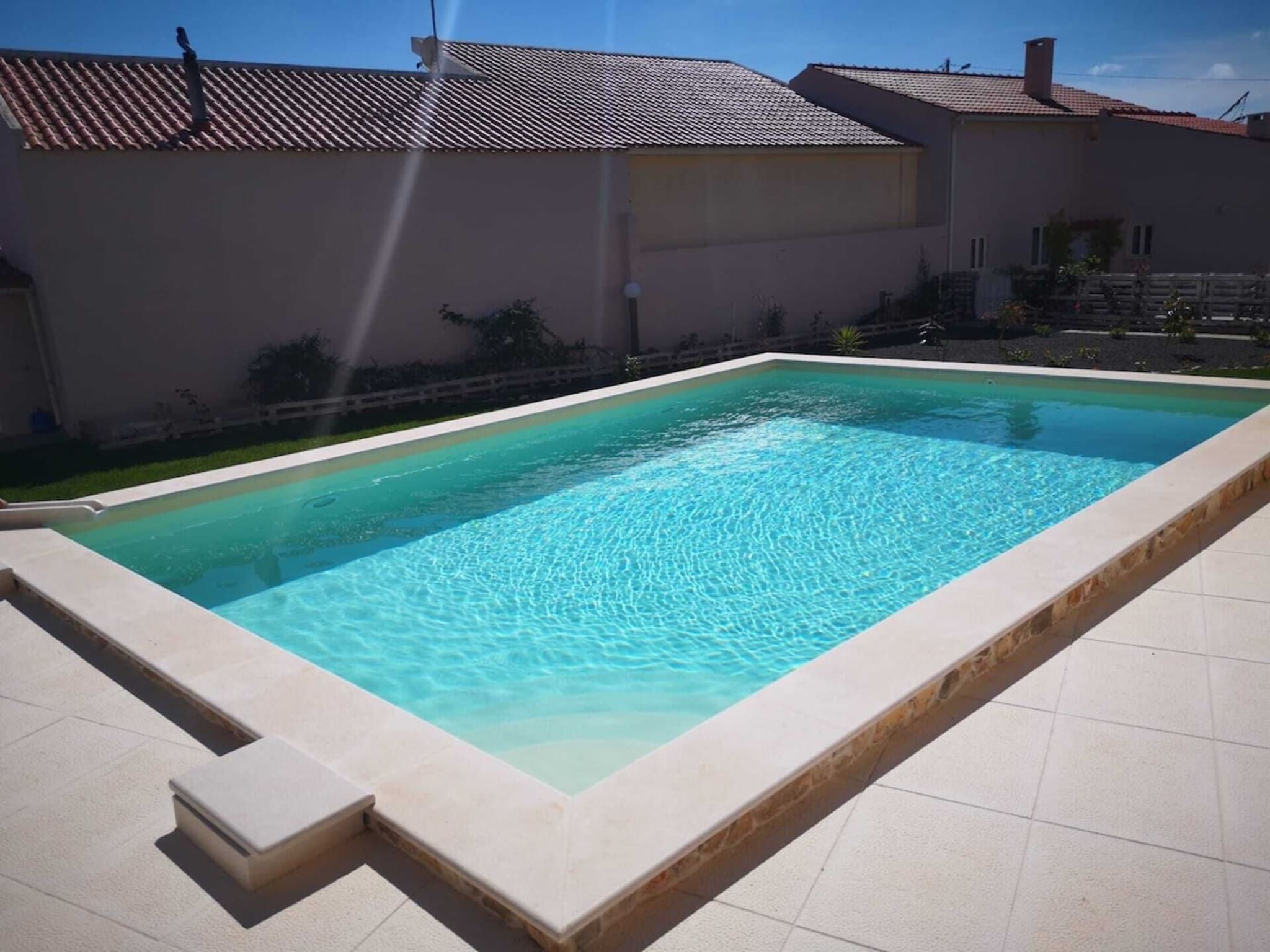 A rectangular swimming pool with a tiled edge, surrounded by a flat roofed building and a clear sky.