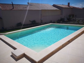 Ein rechteckiger Pool mit einer gefliesten Kante, umgeben von einem Gebäude mit flachem Dach und wolkenlosem Himmel.