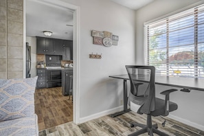 Un espace de vie compact comprenant un coin cuisine, un espace repas avec une table et une chaise, et une fenêtre avec des stores.