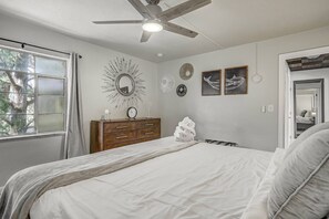 A bedroom with a bed, a dresser, a ceiling fan, and a window with a view of trees. - Pet-Friendly 2BR Penthouse with Mountain Views + Private Deck (Colorado Springs)