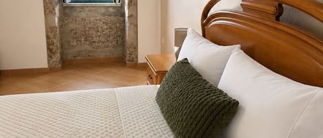 A bedroom with a large bed, a wooden headboard, a view through a window, and a nightstand with a lamp.
