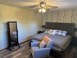 A bedroom with a bed, a chair, a mirror, a ceiling fan, and a wall with a tree pattern. - Casa de la Playa - Walk to the beach (Rimbey)