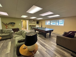 A room with a ping pong table, a sofa, a lamp, and a window with a view. - Casa de la Playa - Walk to the beach (Rimbey)