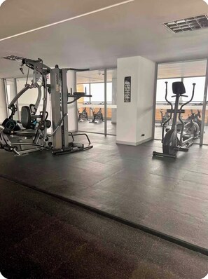 A gym with cardio machines, weightlifting equipment, and a large window providing natural light. - Luxury 3BR Panoramic Views – El Tesoro Medellín (Medellín)