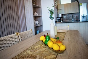 Et spisebord med en vævet bordskåner, en vase med en plante, og en skål med citroner og en pære.