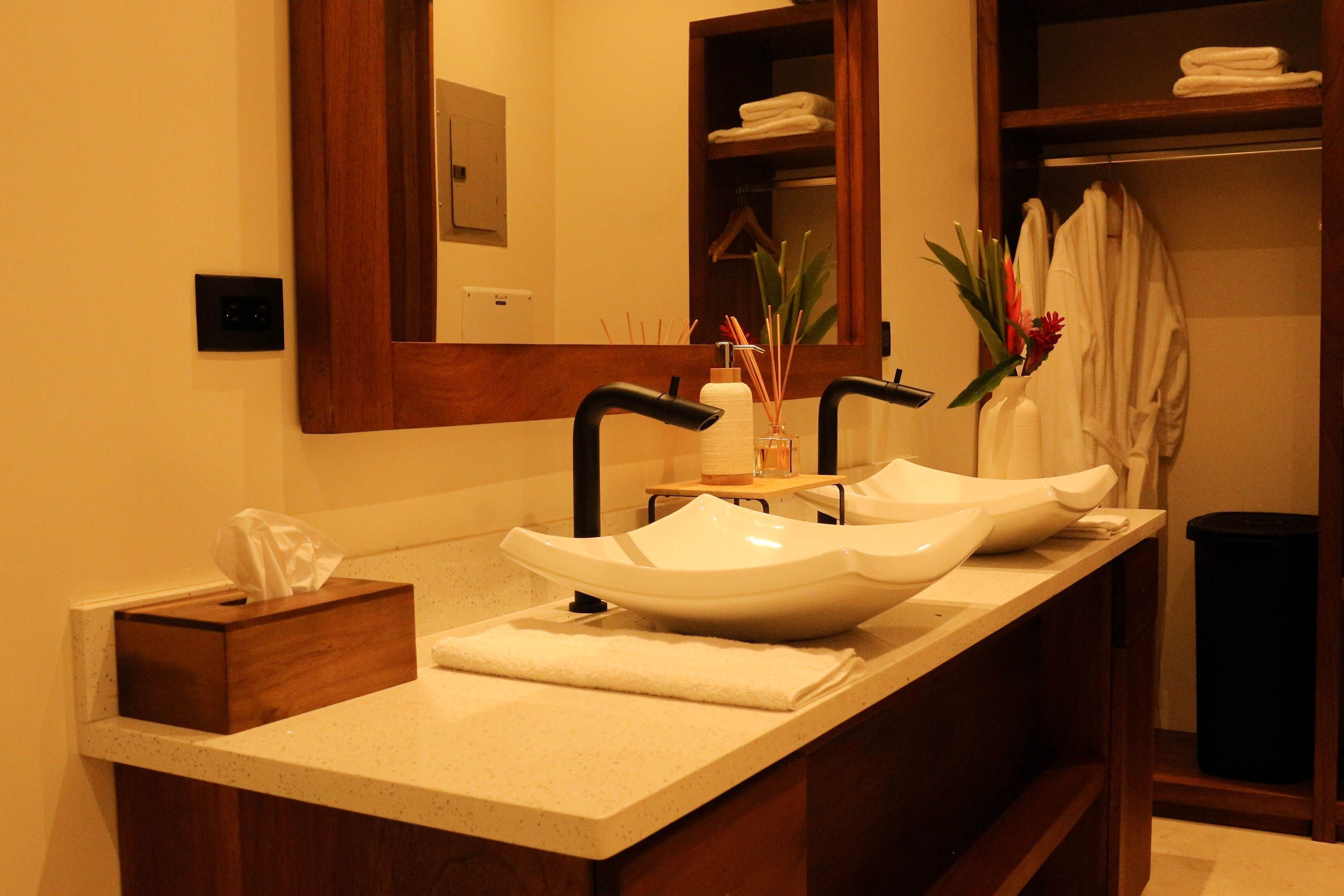 A bathroom with a double sink, a mirror, a towel rack, and a trash bin.