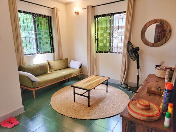 A room with a sofa, a round woven rug, a wooden table, a standing fan, and a mirror on the wall.