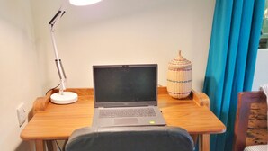 Ein kleiner Arbeitsplatz mit einem Laptop, einer Schreibtischlampe, einem Korbwäsche und einem Stuhl.