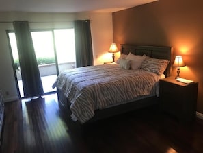 Une chambre à coucher avec un lit, deux tables de chevet avec des lampes, une fenêtre avec des rideaux et une vue sur l’extérieur.