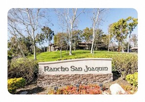 A sign for Rancho San Joaquin with a stone base and a grassy hill in the background.