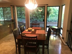 A dining area with a table and chairs, large windows, and a view of greenery.