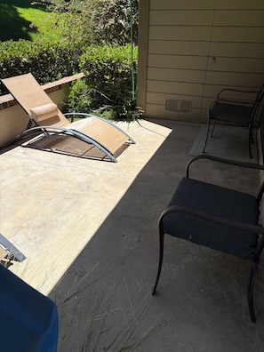 A patio area with a concrete floor, a metal chair, and a lounge chair.