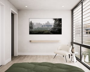 Quarto moderno com uma grande janela, um quadro pendurado, uma cadeira, uma mesinha e um tapete verde.