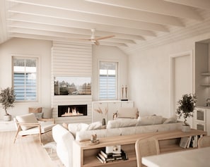 Uma sala de estar ampla com lareira, ventilador de teto e vista para o exterior através de grandes janelas.