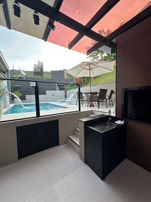 A modern outdoor kitchen area with a pool, a dining set, and a view of the surrounding landscape.