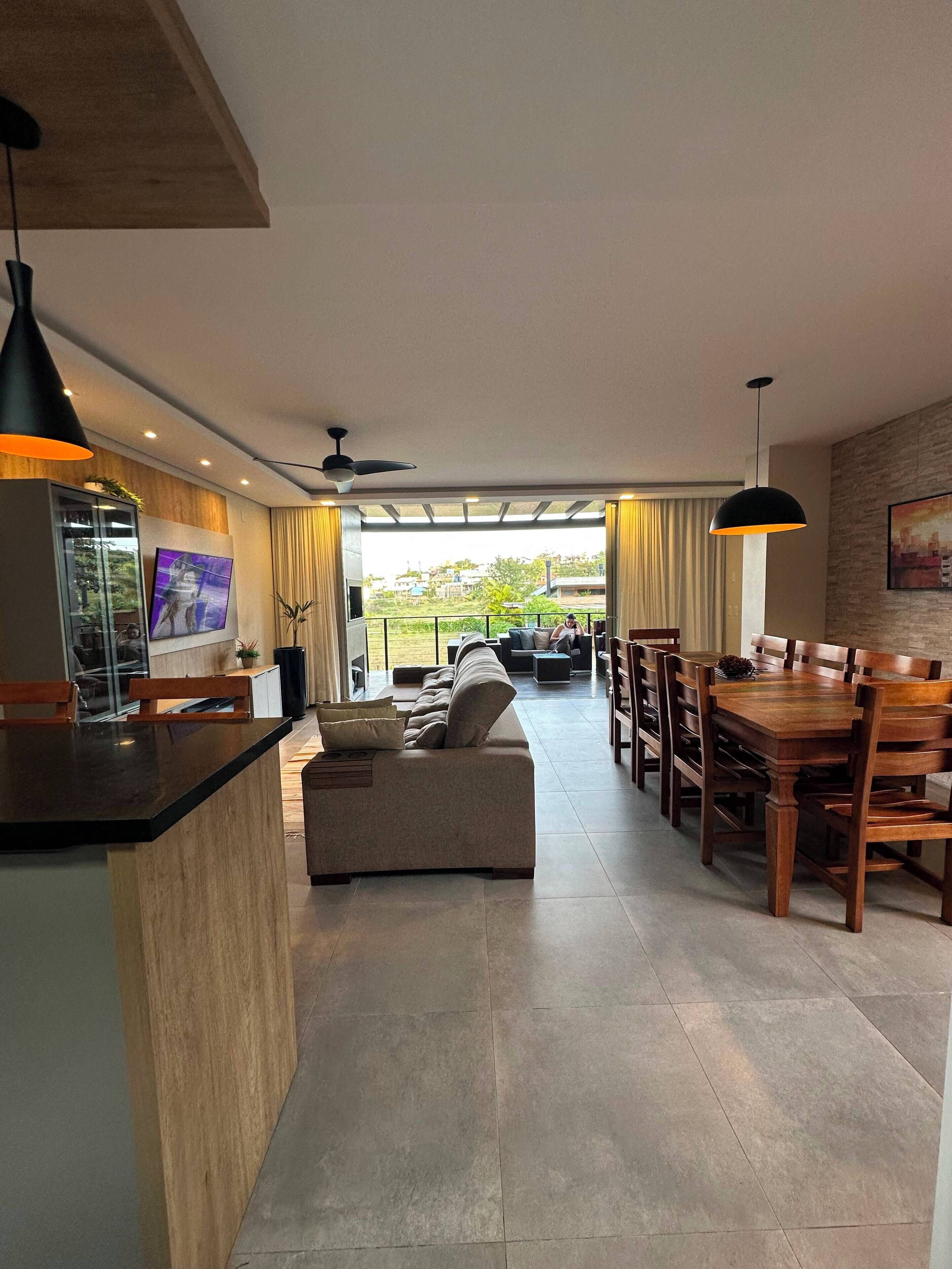 A modern living area with a sofa, dining table, and chairs, a kitchen area with a counter, and a view through a glass door.