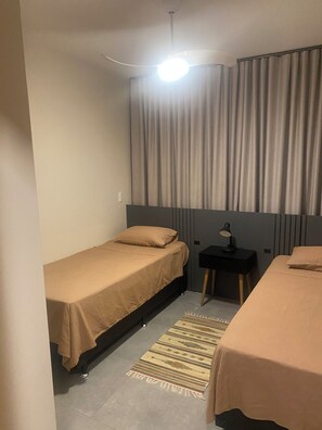 A small, single-bed room with a bed, a nightstand, a lamp, and a window with curtains.