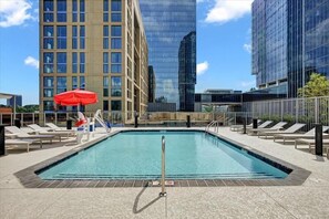 A rooftop pool with lounge chairs, a red umbrella, and modern buildings in the background. - New! Petfriendly, Reston 3BR near Metro (Reston)