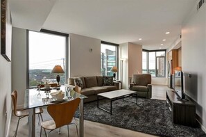 Un salon moderne avec une table à manger en verre, un canapé, une table basse et un téléviseur.