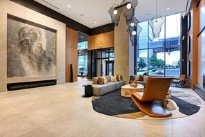 Un vestíbulo moderno con una gran escultura abstracta, una zona de estar con sofás y una mesa de centro, y ventanas amplias que ofrecen vistas al exterior.