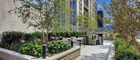 An outdoor patio area with seating, plants, and a modern building in the background.