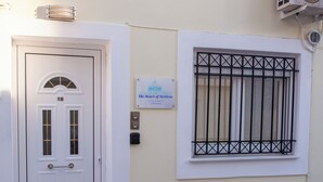 Uma porta branca com placa de identificação, uma janela com grade de metal e um letreiro indicando 'The Heart of Mytilene - Apartment -'.