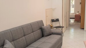 Uma sala de estar moderna com um sofá cinza, um objeto decorativo na parede e um corredor que dá para outro quarto.