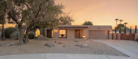 A modern two-story house with a garage, a driveway, and a well-maintained front yard with rocks and a tree.