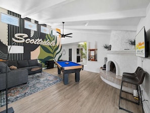 Ein modernes Wohnzimmer mit Billardtisch, einer Couch, einem Kamin und einem Wandgemälde mit dem Schriftzug 'Scottsdale'.