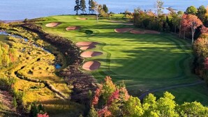 A golf course with a lake in the background, surrounded by autumn-colored trees.
