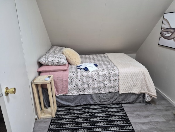 A bedroom with a bed, pillows, a blanket, a small wooden stool, and a black and white striped rug.