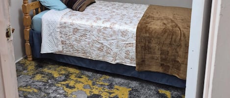 A small, single-bed room with a sloped ceiling, a wooden headboard, and a patterned bedspread.