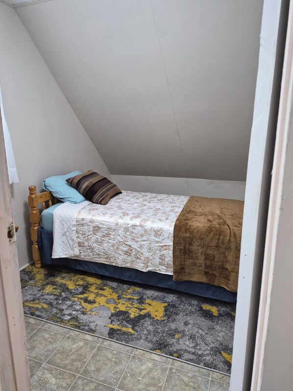 A small, single-bed room with a sloped ceiling, a wooden headboard, and a patterned bedspread.
