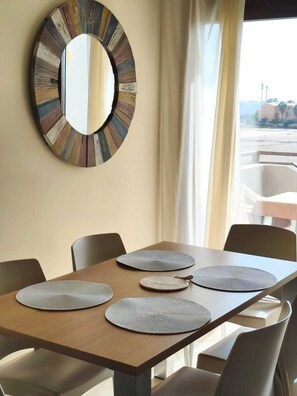 A dining area with a wooden table, four woven placemats, and a large mirror with a wooden frame. - HostySpot - Tropical Resort, 2-Bedroom Apartment (Santa Maria)