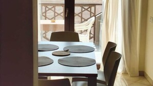 A dining area with a table set for four, chairs, and a view of a distant landscape through a balcony door. - HostySpot - Tropical Resort, 2-Bedroom Apartment (Santa Maria)