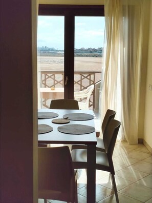 A dining area with a table set for four, chairs, and a view of a distant landscape through a balcony door. - HostySpot - Tropical Resort, 2-Bedroom Apartment (Santa Maria)
