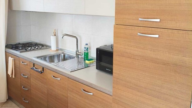A kitchen with wooden cabinets, a stainless steel sink, a microwave, and a gas stove. - HostySpot - Tropical Resort, 2-Bedroom Apartment (Santa Maria)