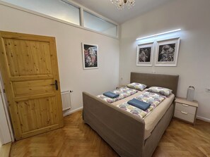 Een slaapkamer met een houten deur, een bed met beddengoed met een patroon, een nachtkastje en een radiator.