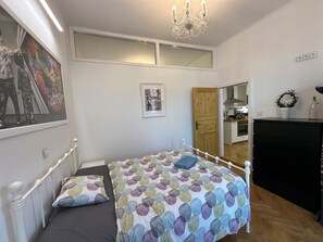 Ein Schlafzimmer mit einem Bett, einer Chandelier, einem Gemälde, einer Tür und Blick zur Küche.